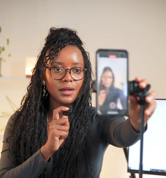 a woman is filming herself using an iPhone, on a tripod, and holding a microphone. Full time Content Creator