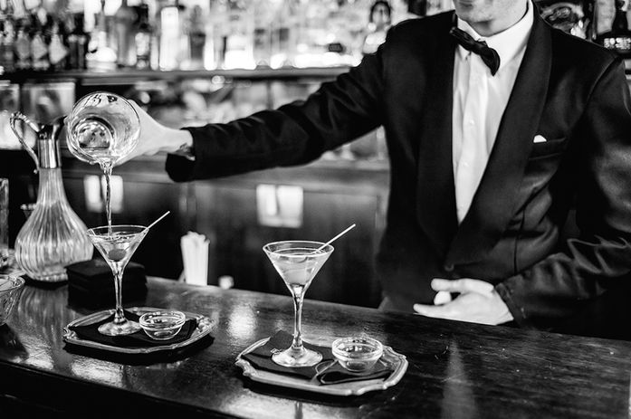 A black and white photo of the bartender serving cocktails in a martini glass.