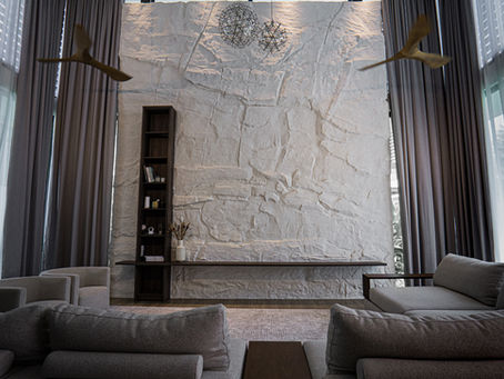 An expansive double-volume living room in Kuala Lumpur featuring a hand-troweled natural stone mineral wall highlighted by warm architectural downlighting