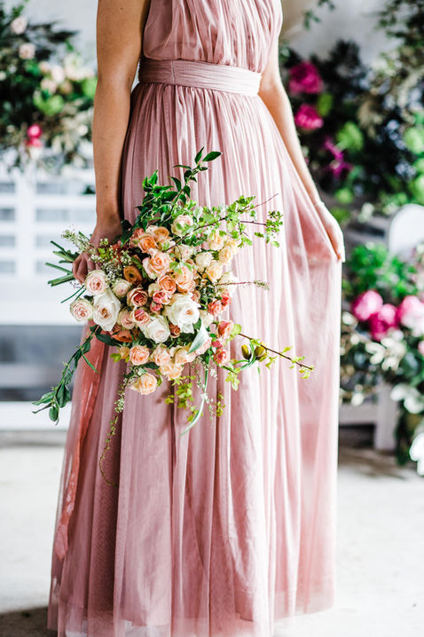 Bride in pink wedding dress holding bouquet made of different roses and greenery at Ledbury Herefordshire.