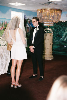 groom wearing black tuxedo smiles in front of mural wall 