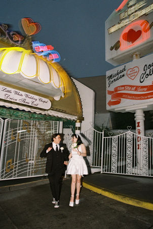 bride and groom wearing wedding attire take photos outside of the little white wedding chapel in las vegas at night with neon signs