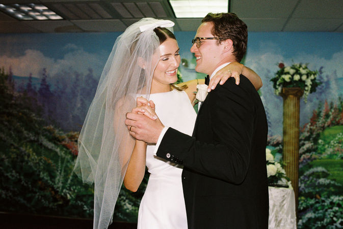 bride and groom stand at altar and smile with murals and chandeliers behind them at the little white chapel