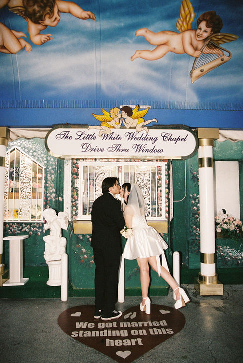 bride and groom wearing wedding attire hold hands in the tunnel of love at the little white wedding chapel with cupid mural overhead