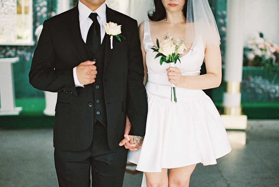 bride and groom wearing wedding attire hold hands and pose, picture from nose to knees. bride holds flowers