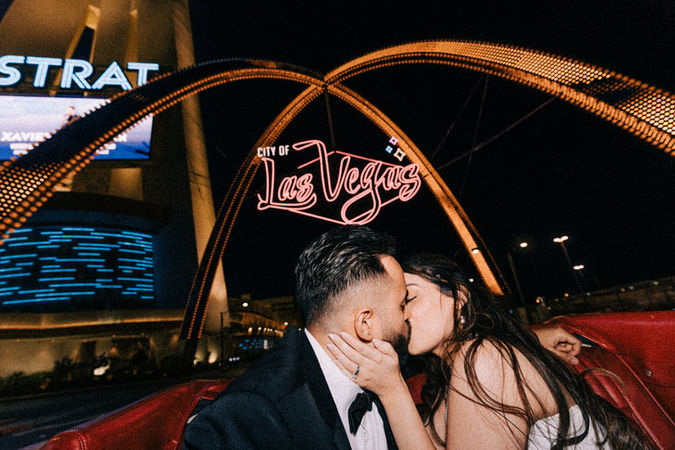 Bride and groom kiss under the neon las Vegas sign. Rent a vintage wedding car. Bride and groom drive the Las Vegas Strip at night in classic convertible mustang. Best places to take wedding day pictures in Las Vegas. captured by las Vegas elopement photographer brazen honey films