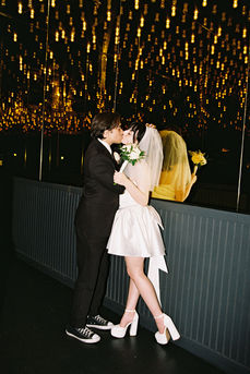 bride wearing white dress embraces groom while holding flowers and smiling underneath golden neon lights