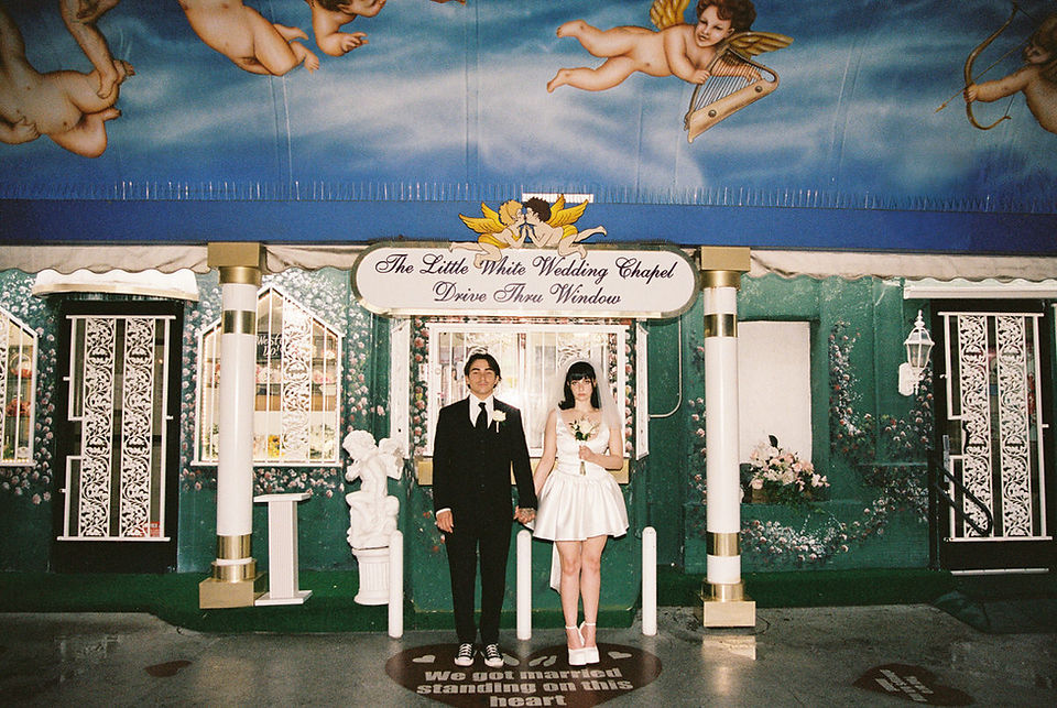 bride and groom wearing wedding attire hold hands in the tunnel of love at the little white wedding chapel with cupid mural overhead