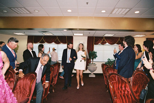 bride and escort walk down the isle at the little white chapel amore with red carpets and couches