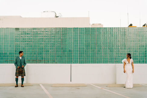 Bride and groom pose for pictures in downtown las vegas at golden hour with the strip in the background. captured by las vegas wedding photographer brazen honey films. Groom wears stylish stottish kilt. Bride wears custom made with love bridal gown.