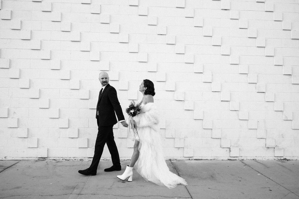 black and white photograph of bride and groom walking down fremont street in las vegas on their wedding day. captured by las vegas elopement photographer brazen honey films