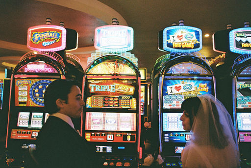 bride and groom look at each other sitting in front of slot machines in las vegas