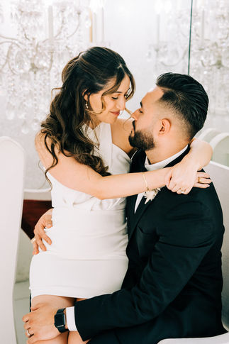 Bride and groom share an embrace at the little white wedding chapel. Bride wears white mini dress, posing in front of a chandelier. Captured by las Vegas elopement photographer brazen honey films.