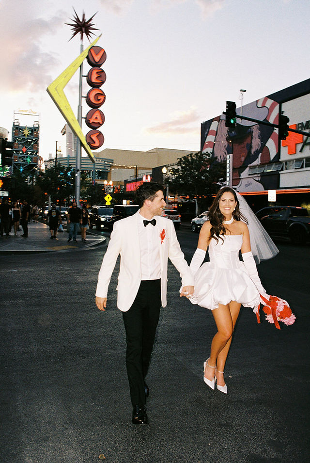 Las Vegas film photographer brazen honey films captures couple from New Zealand who got married at the little white wedding chapel. Bride wears short white gown with red and pink florals from Lucid Juliet. 35mm film photos taken under colorful murals and neon lights.