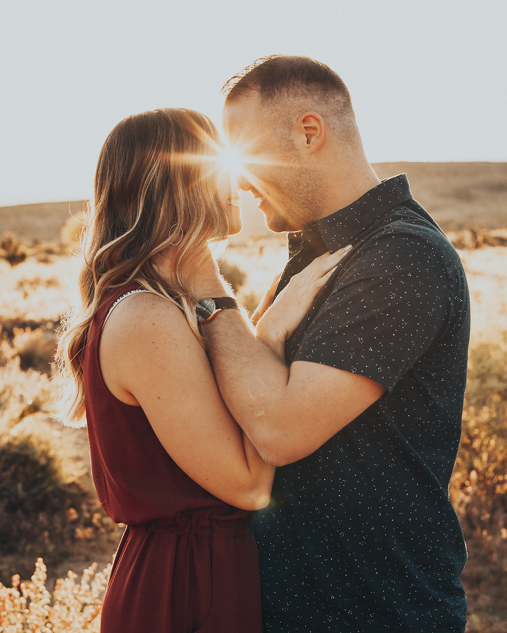A couple hold each other and laugh together at sunrise in the desert surrounded by cactus and joshua trees. captured by las vegas engagement photographer hayway films