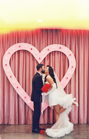 couple wearing wedding attire kissing in front of a pink heart altar at the sure thing chapel