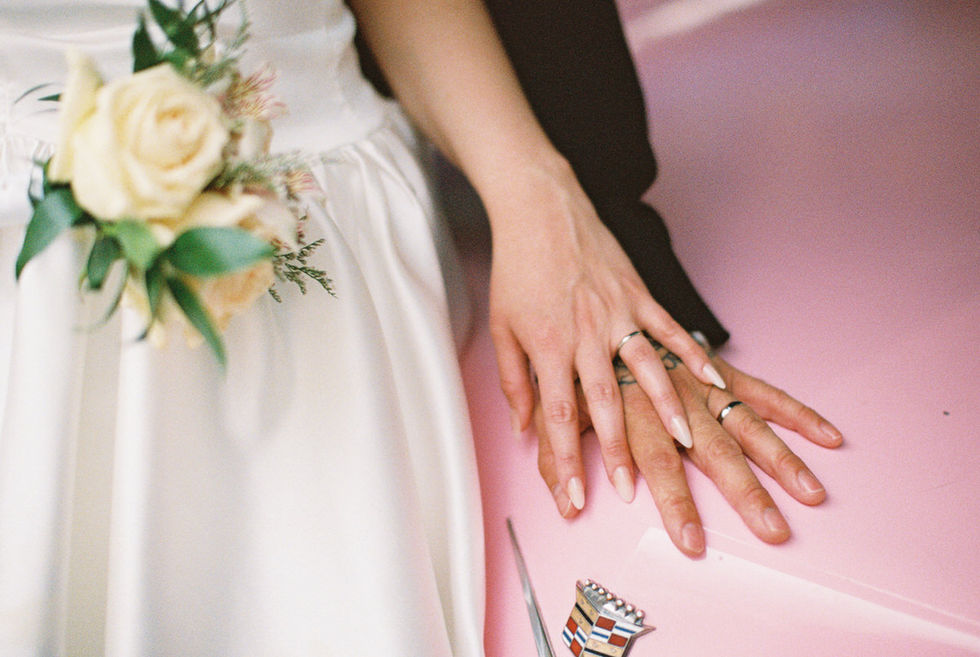 photo of hands with wedding rings sitting on a pink cadillac with white flowers