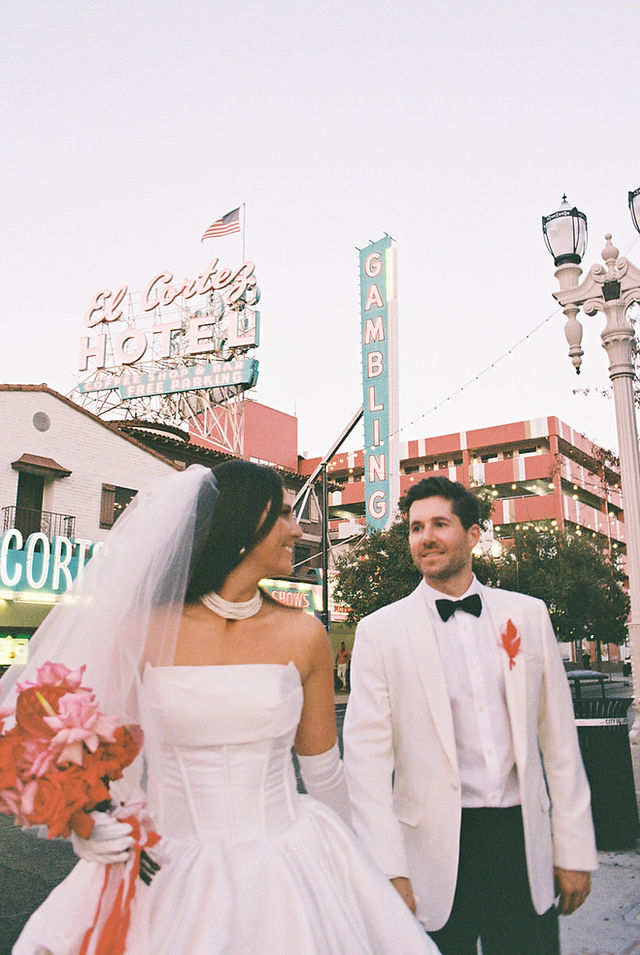 Las Vegas film photographer brazen honey films captures couple from New Zealand who got married at the little white wedding chapel. Bride wears short white gown with red and pink florals from Lucid Juliet. 35mm film photos taken under colorful murals and neon lights.