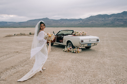 las vegas elopement photographer. Eldorado dry lake bed wedding outside of las vegas. 1966 white mustang with red interior and license plate that says "hitched" is parked in the desert and covered with pastel florals. Vintage convertible car floral installation for wedding photos