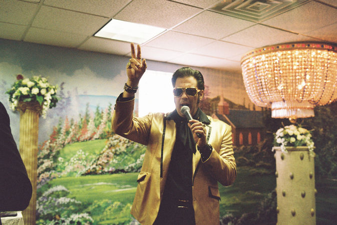 elvis impersonator sings into microphone and raises hand in air