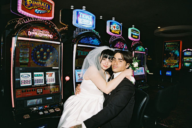 bride wearing white sits on groom lap in front of slot machines smiling