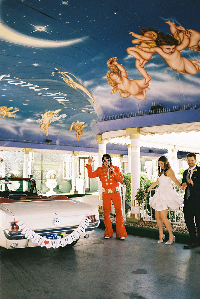 Married couple drives away from the little white wedding chapel in las vegas in a 1966 white convertible mustang after their vegas elopement, captured by las vegas wedding photographer brazen honey films
