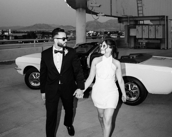 Black and white portrait of bride and groom holding hands, with classic 1966 mustang. Where to take wedding pictures in Las Vegas. Captured by las Vegas elopement photographer brazen honey films.