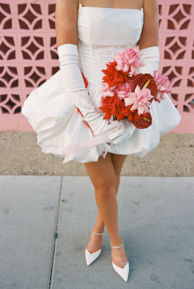 Las Vegas film photographer brazen honey films captures couple from New Zealand who got married at the little white wedding chapel. Bride wears short white gown with red and pink florals from Lucid Juliet. 35mm film photos taken under colorful murals and neon lights.