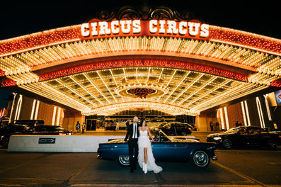 Bride and groom pose under the neon lights in downtown las vegas riding in the back of a convertible blue thunderbird. Captured by las vegas elopement photographer brazen honey films