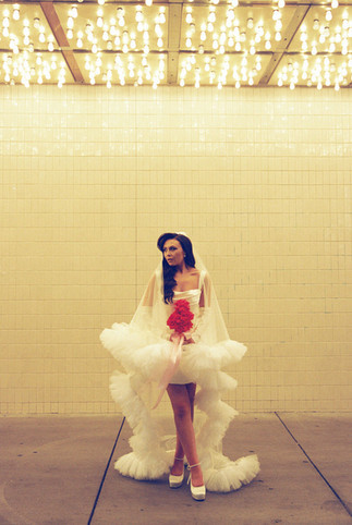 bride wearing long veil with lots of tulle poses with red flowers underneath golden neon lights at the plaza hotel in las vegas