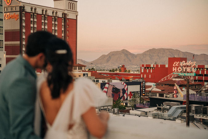 Bride and groom pose for pictures in downtown las vegas at golden hour with the strip in the background. captured by las vegas wedding photographer brazen honey films. Groom wears stylish stottish kilt. Bride wears custom made with love bridal gown.