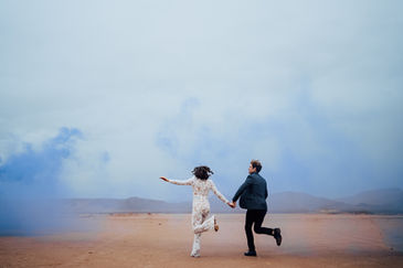 Bride and groom take photos with smoke bombs in the desert on a stormy day. Bride is wearing a Lacey bridal jumpsuit. Captured by Las Vegas wedding photographer brazen honey films
