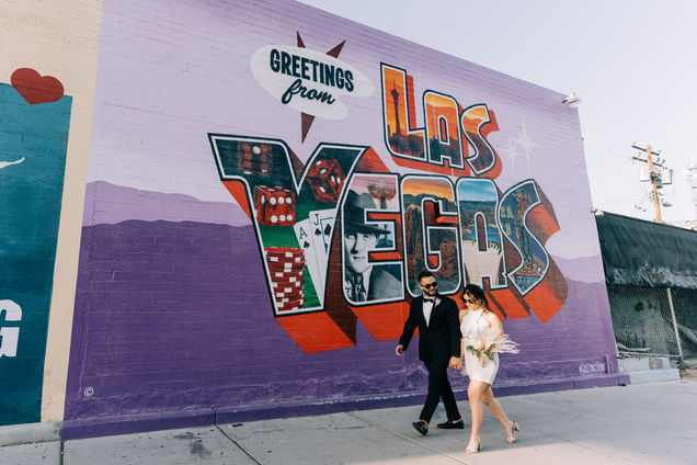 Bride and groom kiss in front of Las Vegas postcard mural in the arts district. Where to take wedding pictures in Las Vegas. Captured by las Vegas elopement photographer brazen honey films.