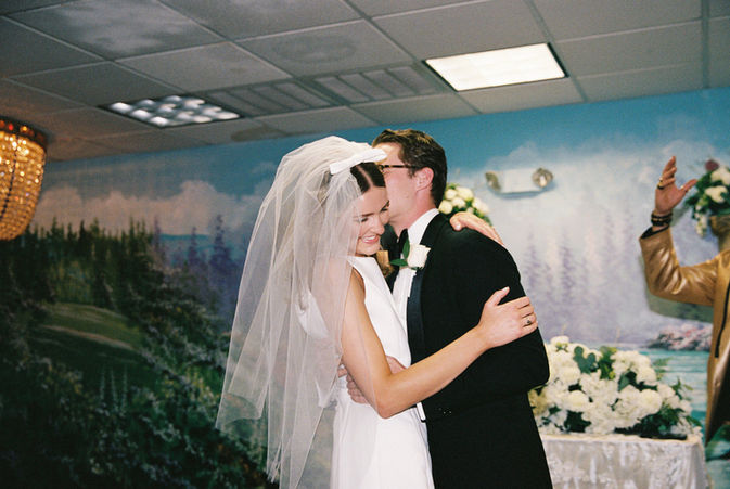 bride and groom stand at altar and smile with murals and chandeliers behind them at the little white chapel