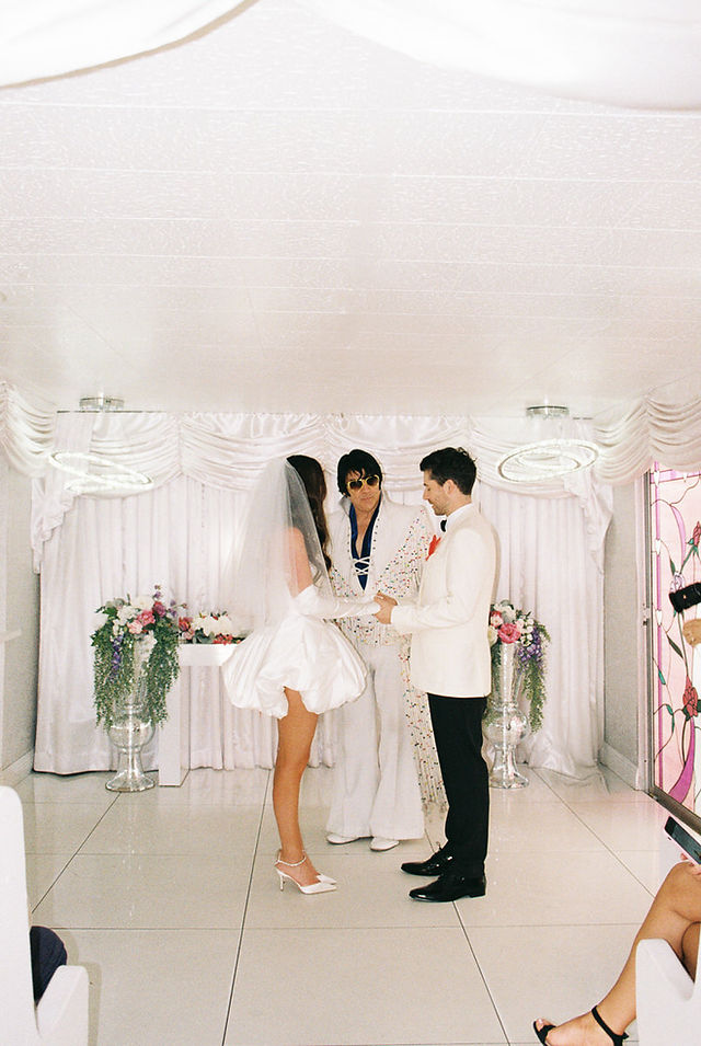 Las Vegas film photographer brazen honey films captures couple from New Zealand who got married at the little white wedding chapel. Bride wears short white gown with red and pink florals from Lucid Juliet. 35mm film photos.