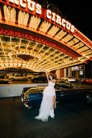 Bride and groom pose under the neon lights in downtown las vegas riding in the back of a convertible blue thunderbird. Captured by las vegas elopement photographer brazen honey films