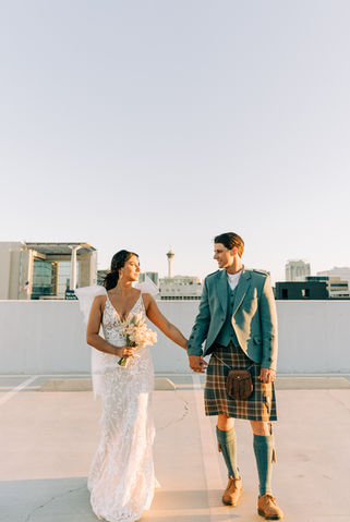 Bride and groom pose for pictures in downtown las vegas at golden hour with the strip in the background. captured by las vegas wedding photographer brazen honey films. Groom wears stylish stottish kilt. Bride wears custom made with love bridal gown.