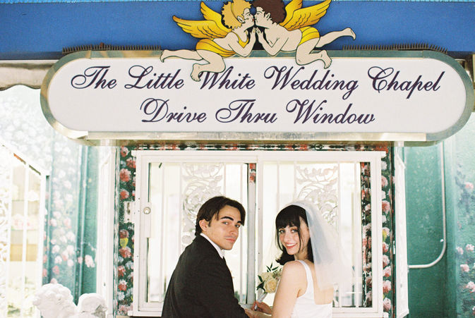 bride and groom wearing wedding attire hold hands in the tunnel of love at the little white wedding chapel with cupid mural overhead