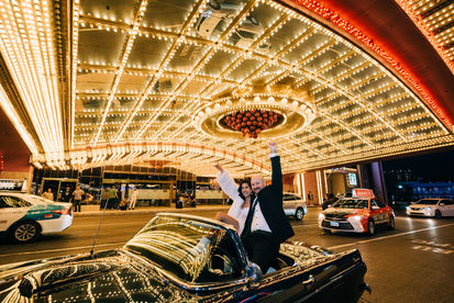 Bride and groom pose under the neon lights in downtown las vegas riding in the back of a convertible blue thunderbird. Captured by las vegas elopement photographer brazen honey films