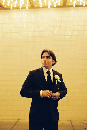 groom wearing black suit poses underneath golden neon lights in downtown las vegas