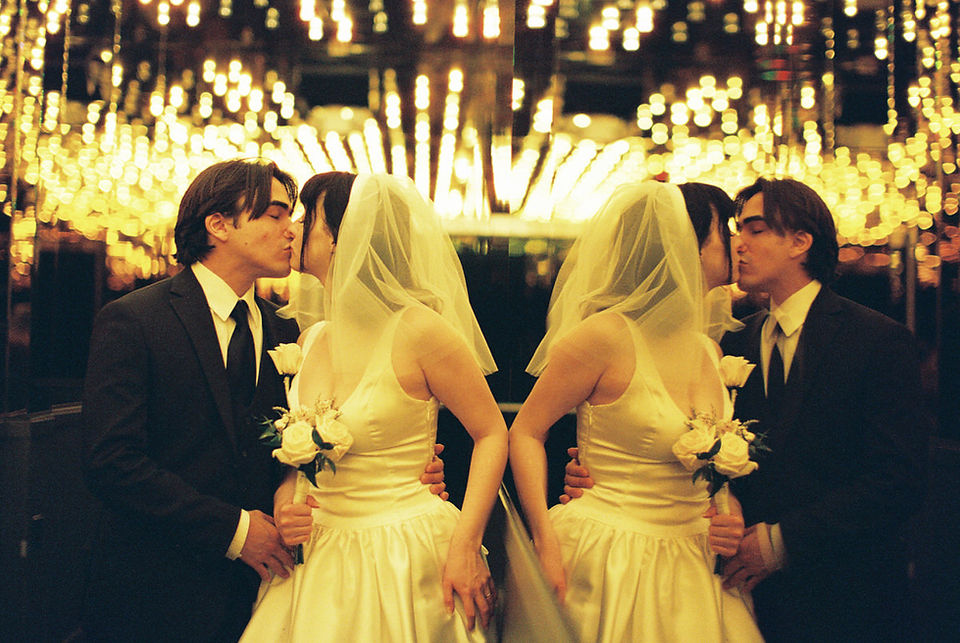 bride wearing white dress embraces groom while holding flowers and smiling underneath golden neon lights