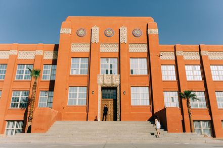 Bride wearing white mini dress walks up to her future husband for a first look in historic downtown Las Vegas. Couple poses in front of large orange building captured by Las Vegas elopement photographer brazen honey films