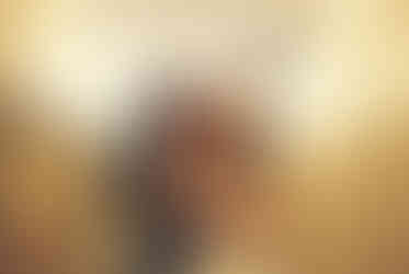 A couple in formal attire joyfully holds hands walking under glowing lights. Background: tiled wall, warm ambiance.