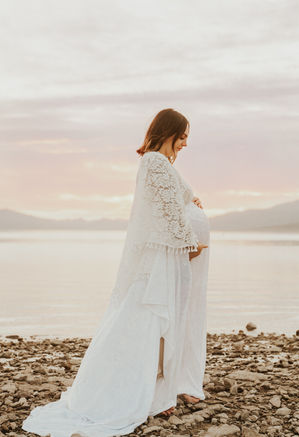 beautiful pregnant mother poses for maternity pictures is reclamation dress over the water at sunrise at lake mead, captured by las vegas family photographer hayway films