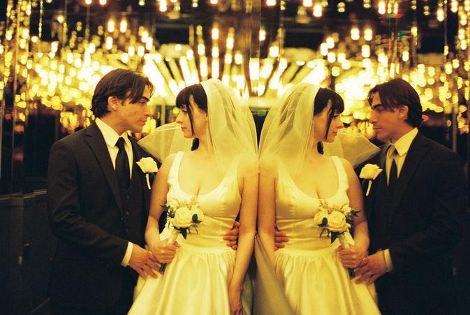 bride wearing white dress embraces groom while holding flowers and smiling underneath golden neon lights