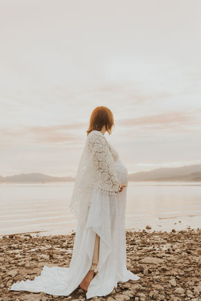 beautiful pregnant mother poses for maternity pictures is reclamation dress over the water at sunrise at lake mead, captured by las vegas family photographer hayway films