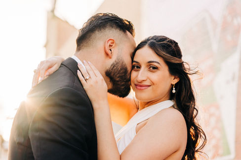Bride and groom hug each other for wedding day portraits. Groom kisses brides face while she smiles into camera. Sun flare during golden hour portraits, captured by Las Vegas elopement photographer brazen honey films
