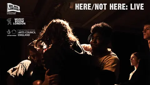 Stage performance scene showing a group of young people embracing in a tight huddle under dramatic theatre lighting. Logos for arts organisations appear at the top, with the title “Here/Not Here: Live” in white text.
