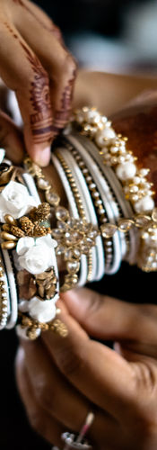 Hands covered in bridal Mehendi, bride-to-be in a cream embroidered wedding dress putting on her jewellery