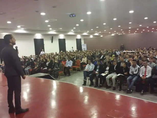 رجل يقف ويتحدث أمام حشد كبير في قاعة المؤتمرات